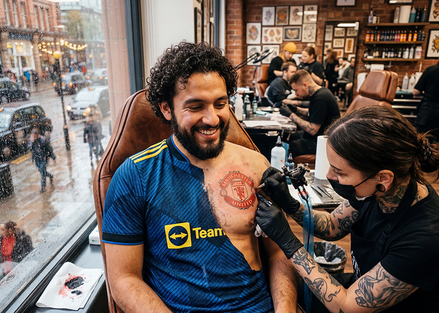 Hombre recibiendo tatuaje del escudo del Manchester United en estudio.