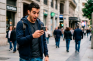 Hombre sorprendido mirando su móvil en una calle concurrida.