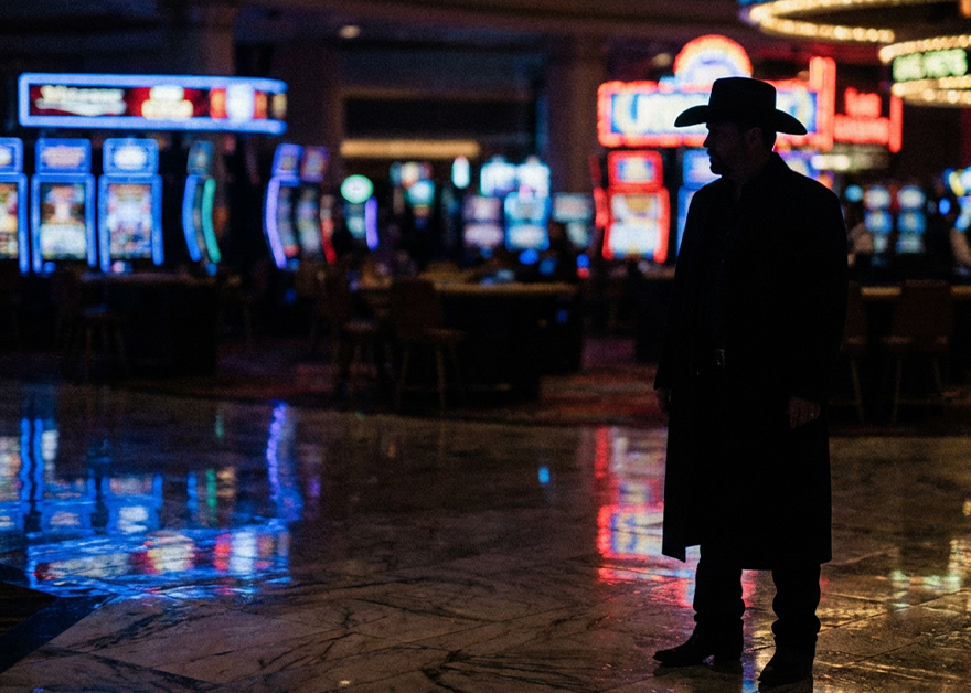 Silueta de hombre con sombrero en un casino, con máquinas tragaperras al fondo.