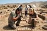 Arqueólogos examinando monedas antiguas en excavación al aire libre.