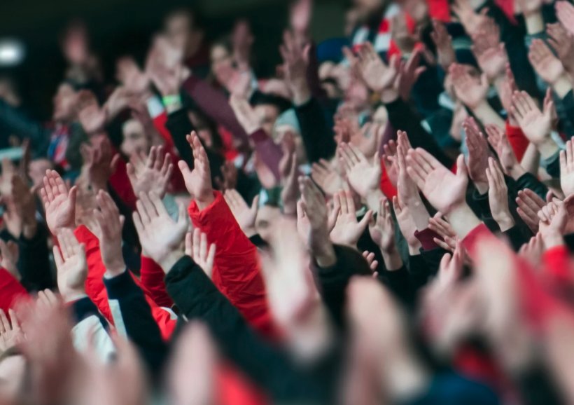 Aficionados de fútbol levantan las manos y aplauden en las gradas durante un partido Copa Mundial de la FIFA.