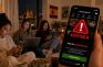 Tres mujeres jóvenes en casa utilizando dispositivos móviles con una advertencia de juego responsable en pantalla.