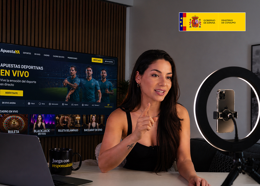 Influencer grabando contenido promocional sobre juego online junto al logotipo del Ministerio de Consumo