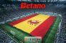 Logos de Betano y Kaizen Gaming sobre una bandera de España desplegada en un estadio de fútbol.