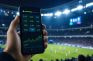 Móvil con cuotas de apuestas y gráficos en directo ante un estadio de fútbol iluminado