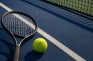 Raqueta y pelota de tenis sobre la pista dura azul de un torneo de Grand Slam
