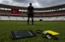 Árbitro en un estadio turco vacío, con un móvil de apuestas y un silbato en el césped